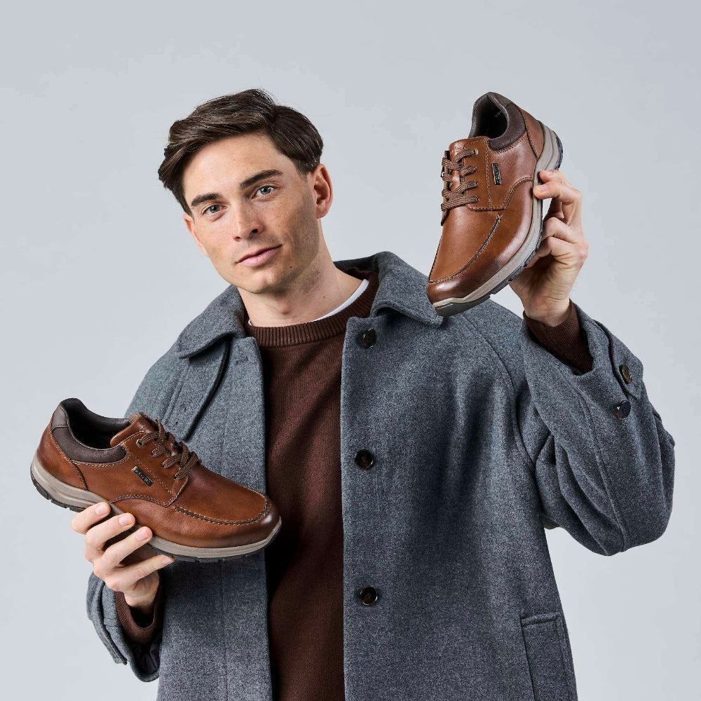 man holding a pair of brown shoes, one in each hand