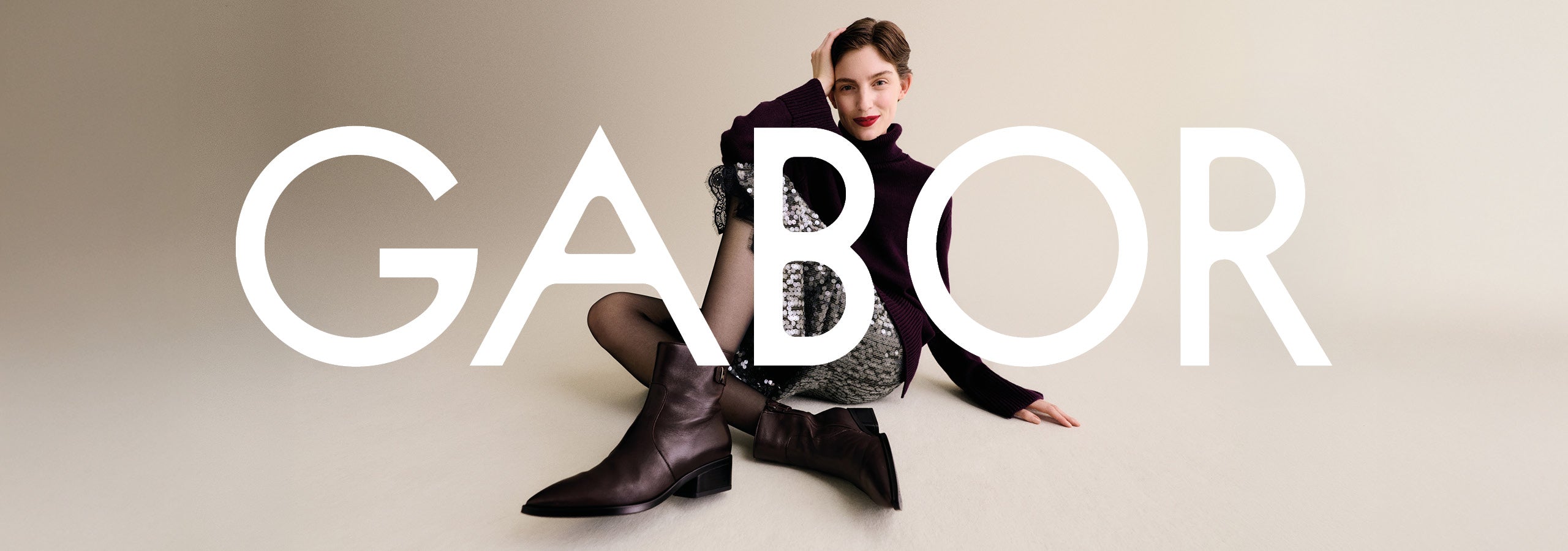 woman sitting on the floor wearing gabor boots with a large gabor logo in front of her